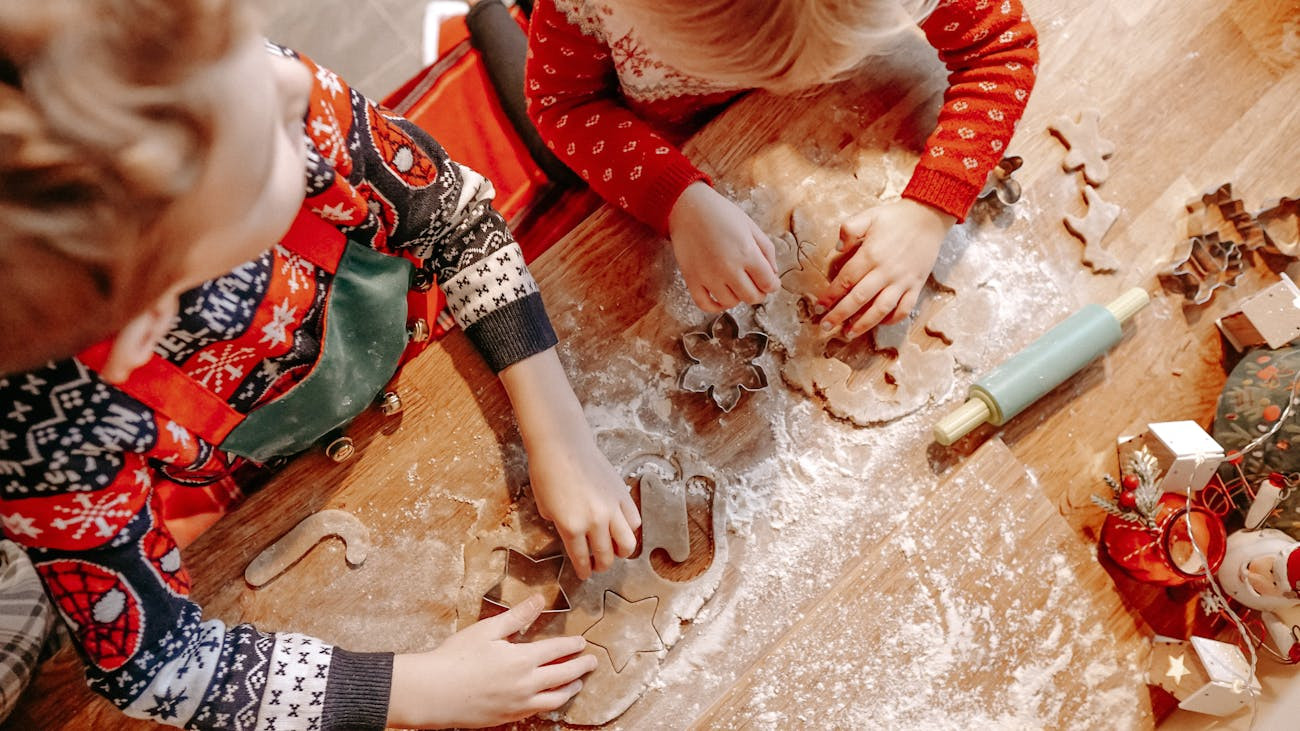 zwei Kinder rollen Teig aus und stechen Kekse aus